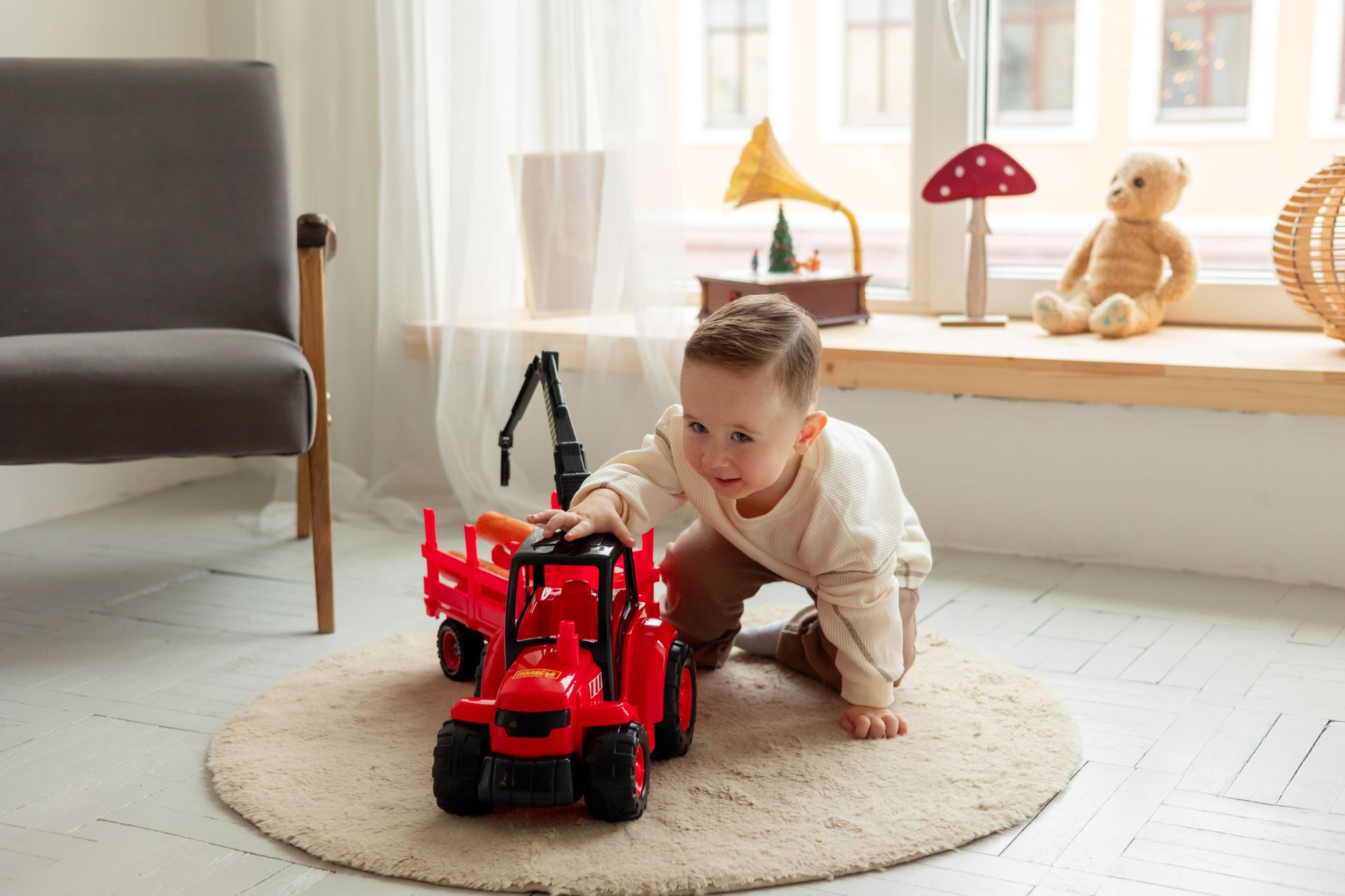 Adorable toddler playing with a red toy tractor on a soft rug in a cozy room.