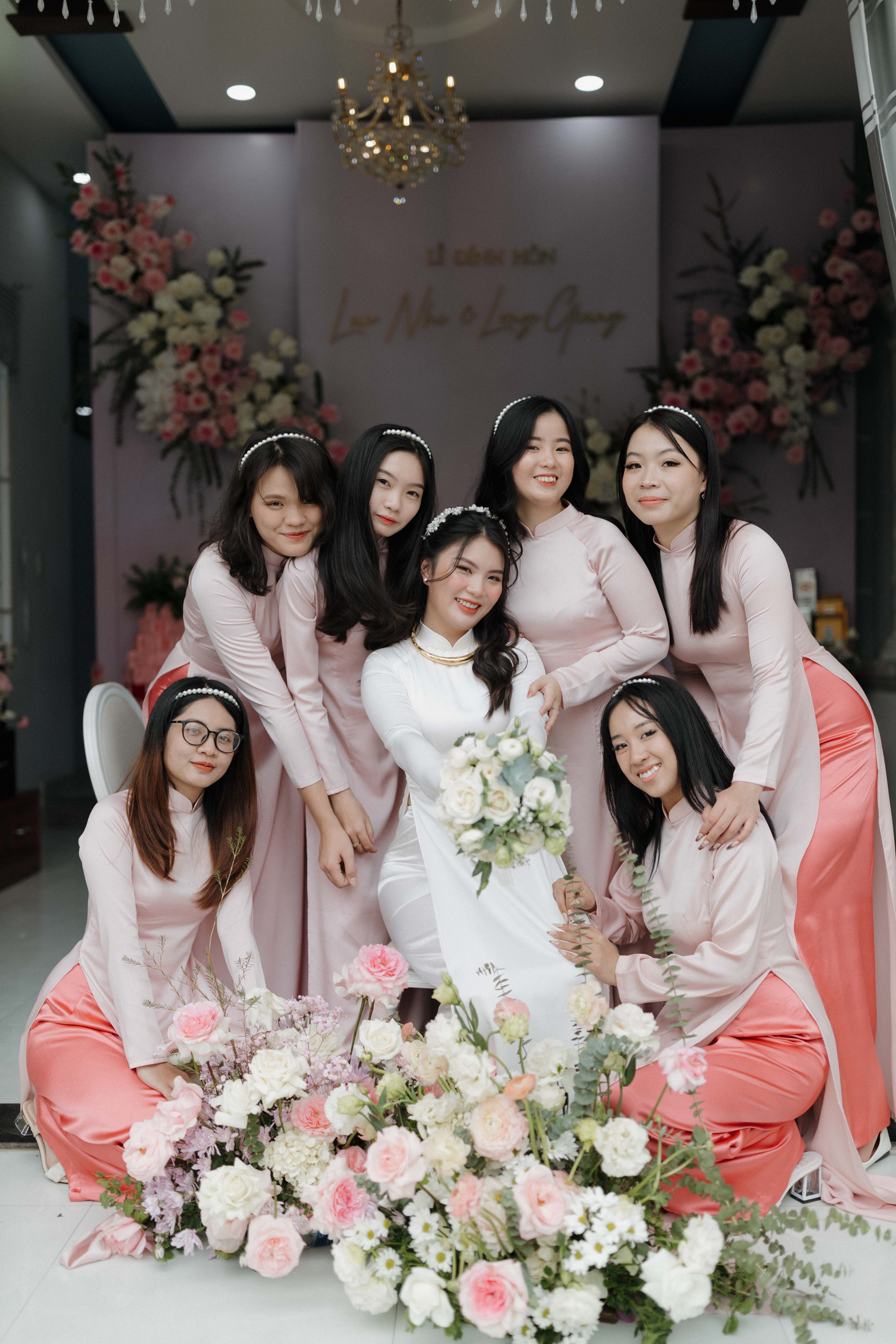 Joyful bridesmaids in pink gowns posing with the bride, surrounded by floral decorations indoors.