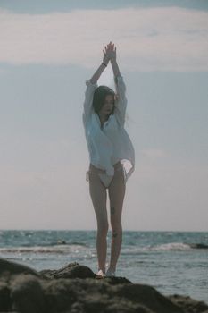 A woman in a white shirt relaxes by the sea, embracing the summer's warm sunlight.