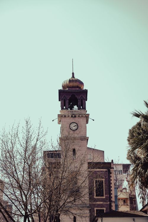Free Clock tower with ornate dome and bare winter trees against a clear sky. Stock Photo