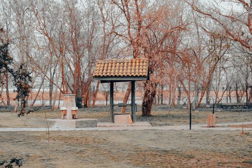 Free A rustic well under a tiled roof amidst leafless trees in an autumn park. Stock Photo