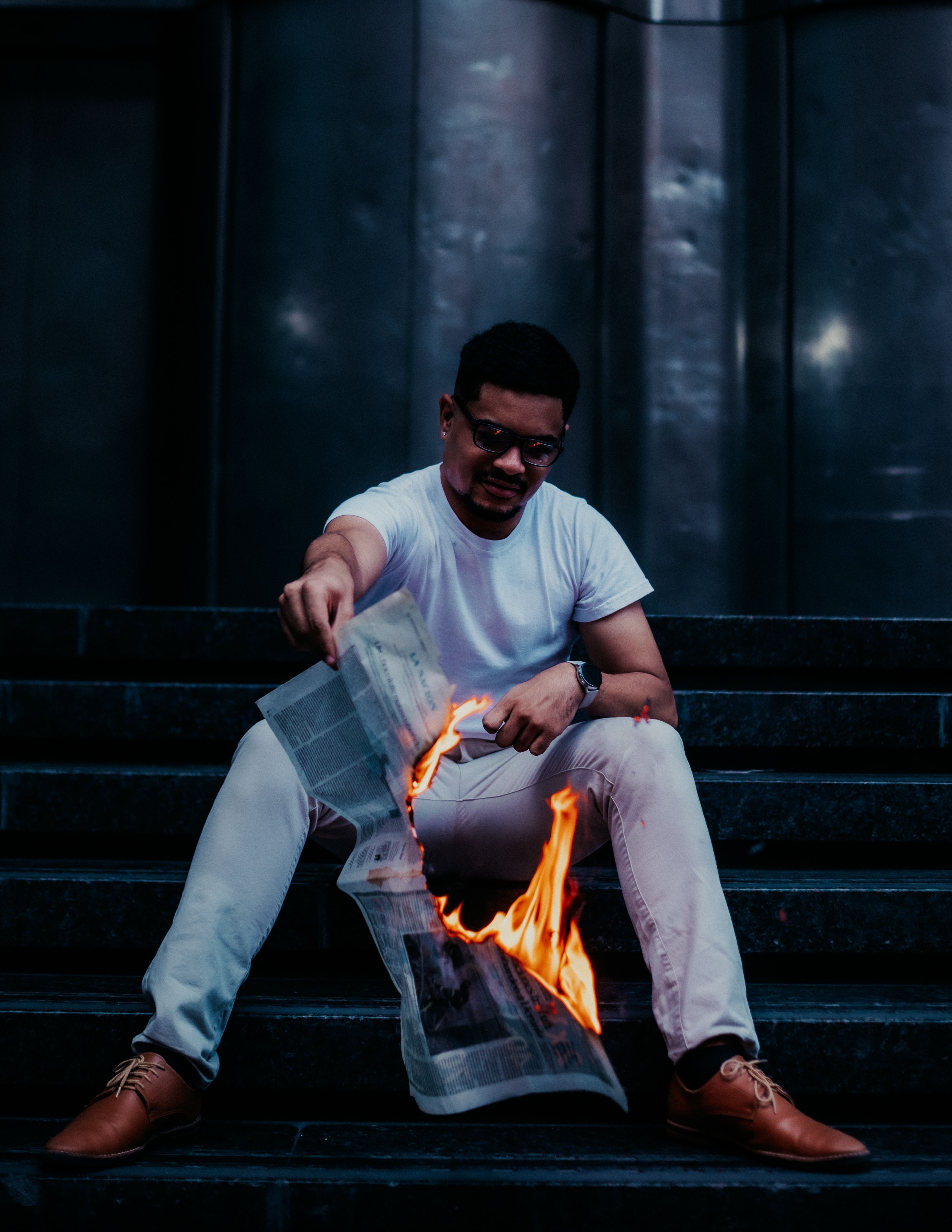 Dramatic portrait of a man burning a newspaper while sitting on urban steps at night.