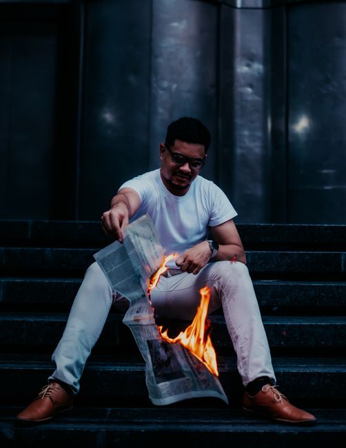 Dramatic portrait of a man burning a newspaper while sitting on urban steps at night. Dramatic portrait of a man burning a newspaper while sitting on urban steps at night.