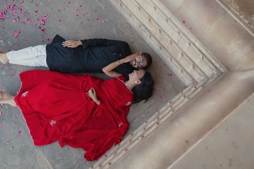 Free Top view of a couple in traditional attire lying on a stone terrace amidst scattered petals. Stock Photo