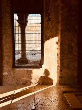 Sunlight casts a dramatic shadow through a window, illuminating a historic stone interior.