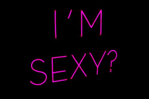 Free Bright pink neon sign displaying the text 'I'm Sexy?' in a dimly lit environment. Stock Photo