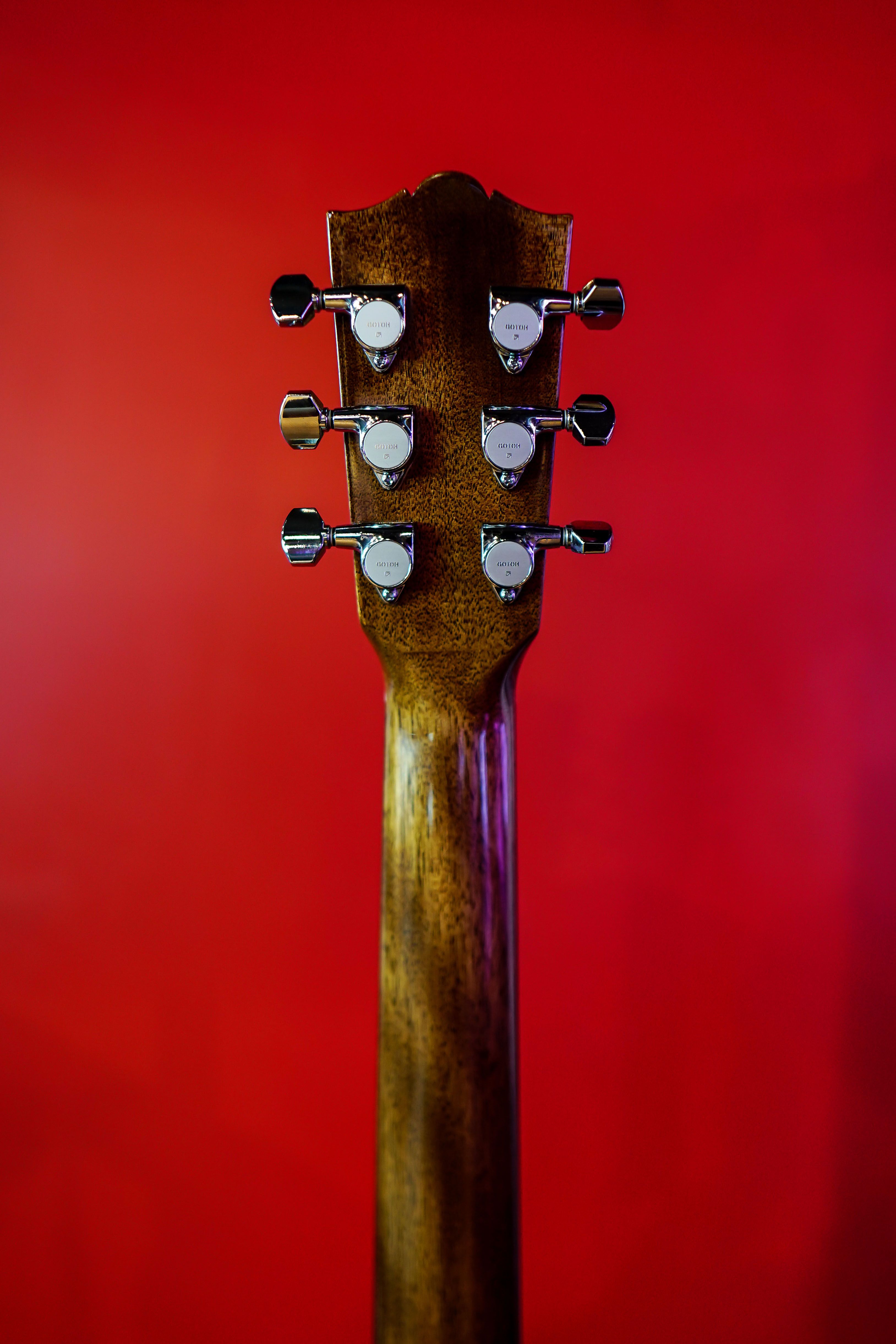 Detailed view of guitar headstock with tuning pegs against a vibrant red background.