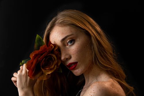 Free A captivating portrait featuring a woman with vibrant makeup and a rose. Stock Photo