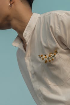 Close-up of a man wearing a white shirt with floral decoration, set against a soft blue background.