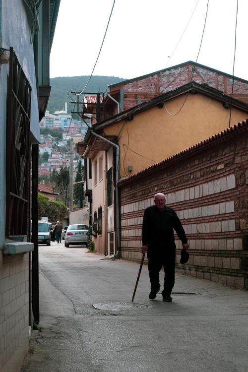 Free An elderly man with a cane walks through a narrow alleyway between buildings in an urban area. Stock Photo