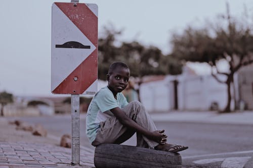 Free Boy Sitting on a Tire Beside Road Signage Stock Photo