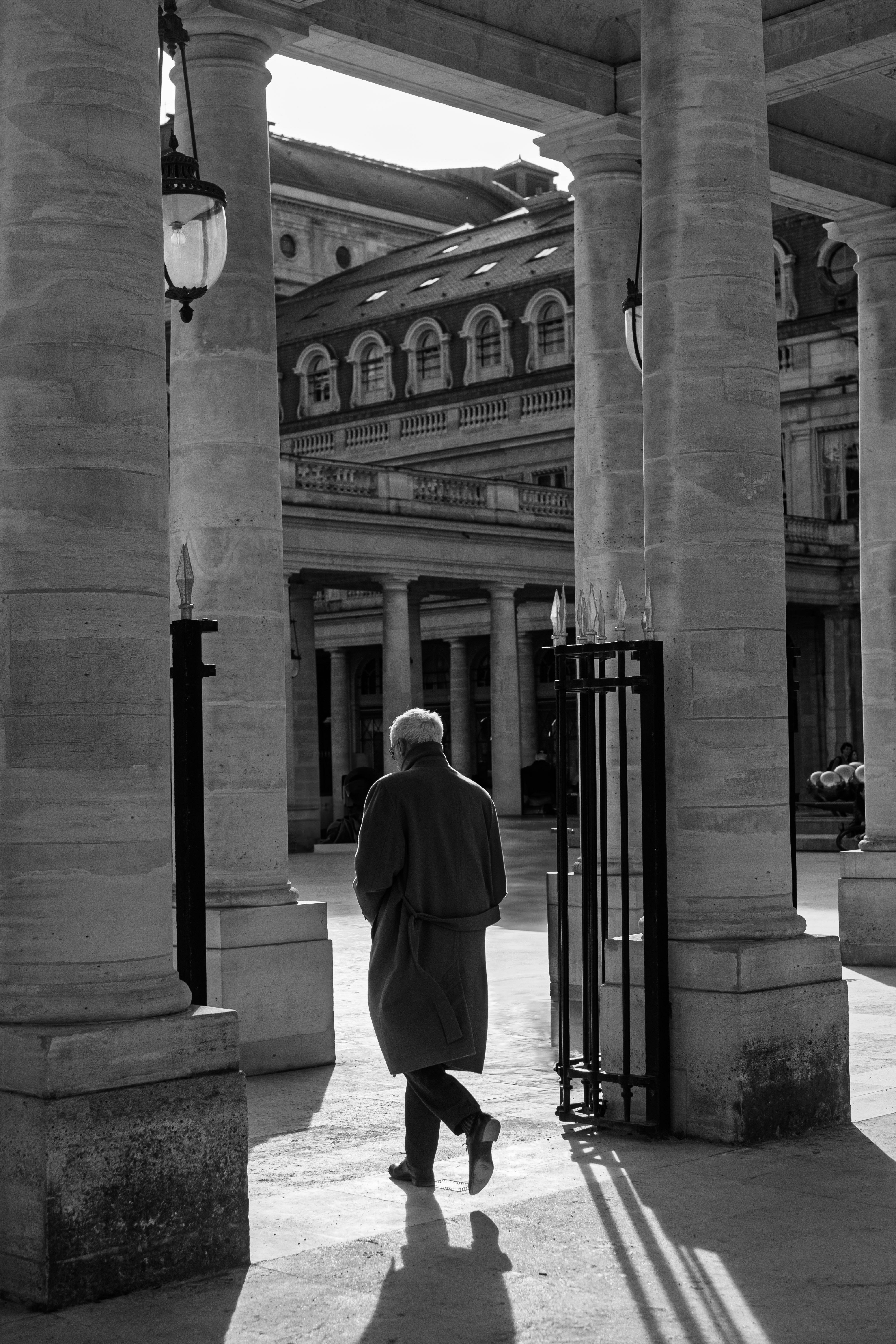 Black and white image of an elderly man walking among classic columns in a historic building.