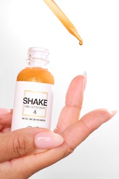 A hand holds a bottle of edible glitter drops, with a dropper releasing a drop.
