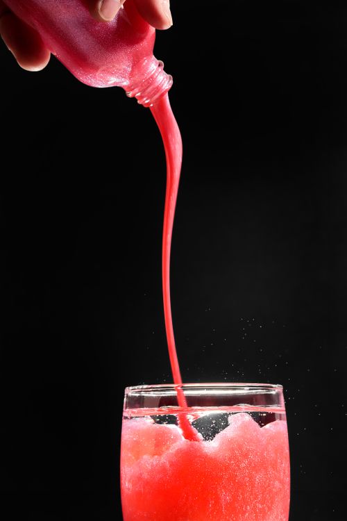 Free A vibrant red non-alcoholic beverage with glitter being poured into a glass, showcasing an artistic effect. Stock Photo