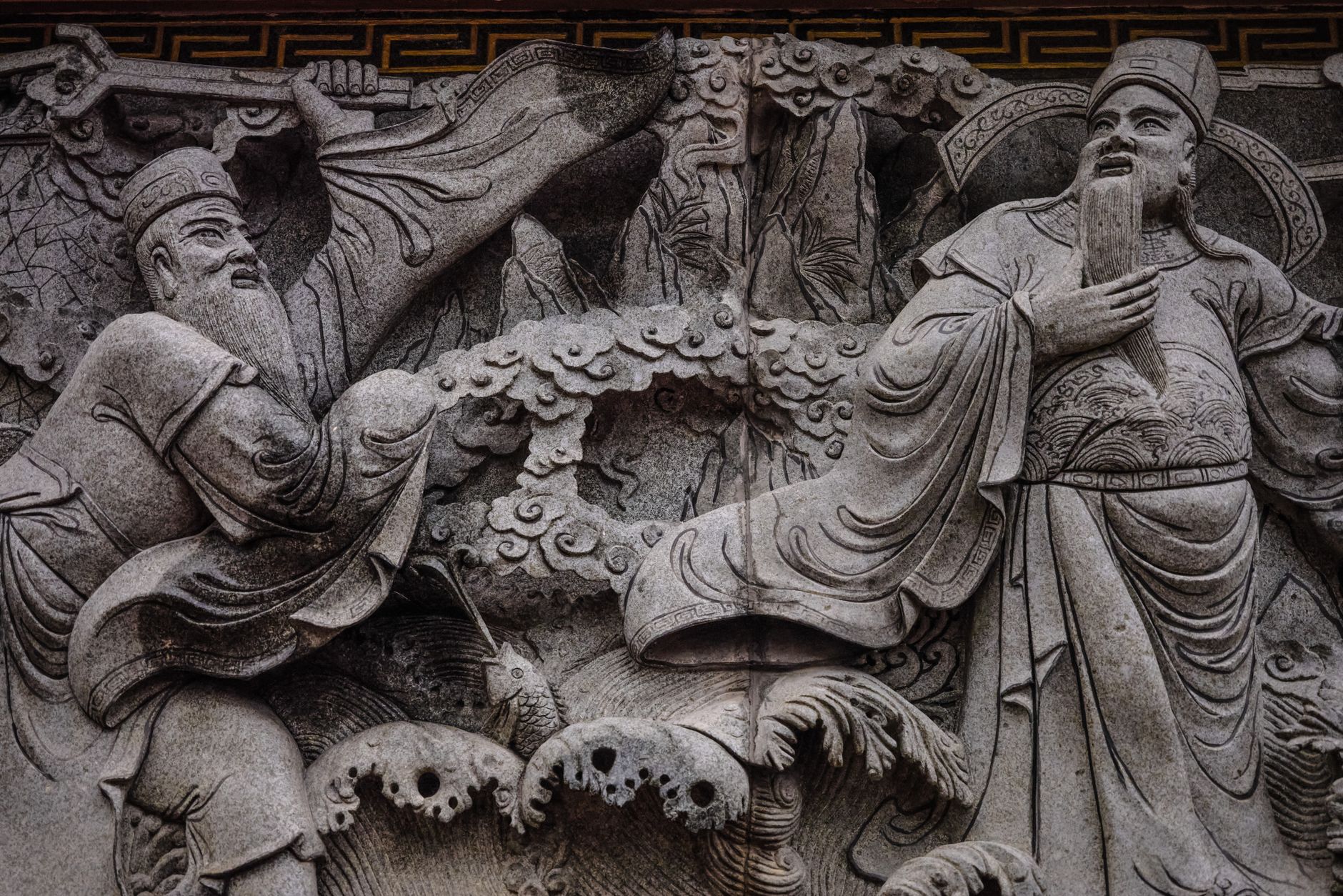 Detailed stone carving depicting ancient oriental figures in traditional attire.