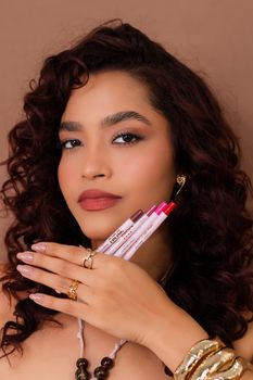 Stylish portrait of a woman holding colorful lip liners, showcasing beauty and fashion.
