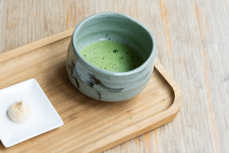 A glazed ceramic cup of matcha on a pale wooden tray