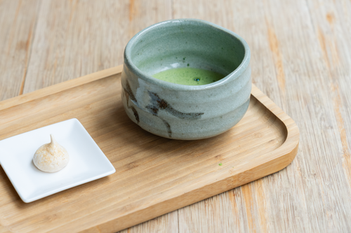 Free Ceramic bowl of matcha tea on wooden tray, accompanied by a small dessert. Stock Photo