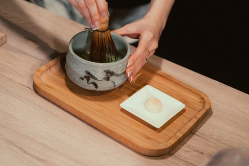 Free Close-up of hands preparing matcha tea using a bamboo whisk and ceramic bowl. Stock Photo