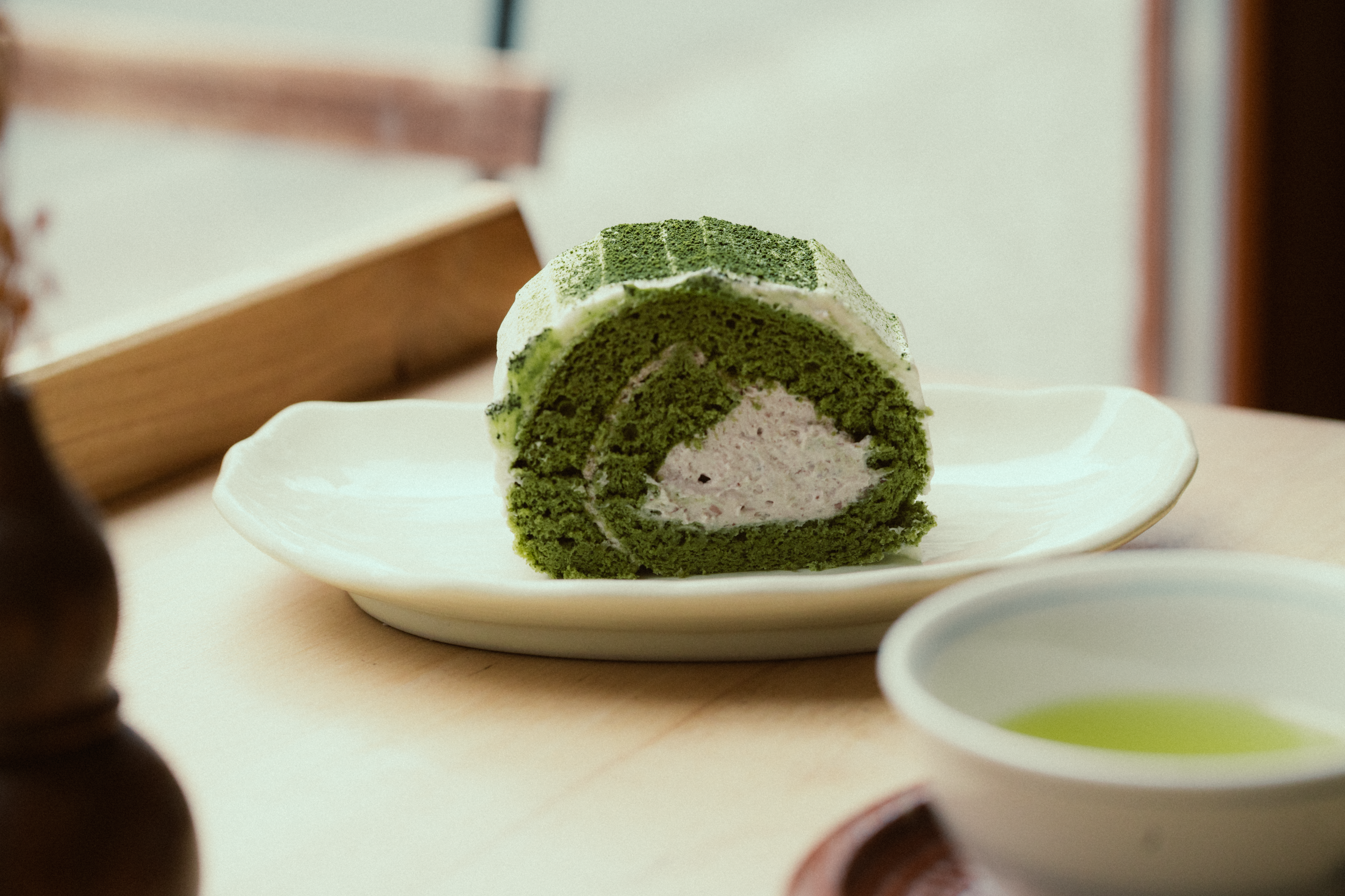 A slice of matcha cake on a white plate with soft lighting