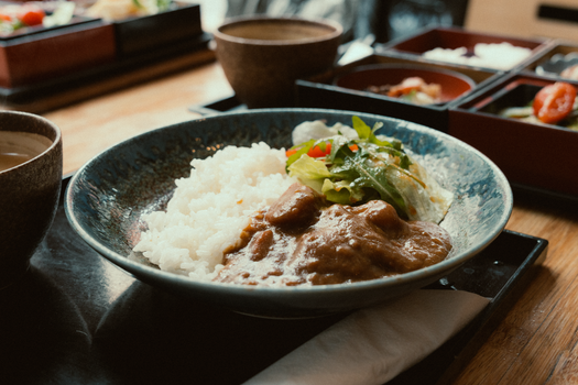 A close-up of a Japanese curry rice dish with salad served in a ceramic bowl.