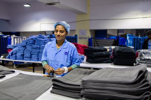 Female worker in a textile factory organizing fabric on tables.