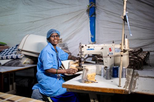 Free Indian textile worker sewing with a smile in a factory setting, showcasing blue-collar work. Stock Photo