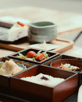 Close-up of a traditional bento box with various Japanese foods, small plates, and tea.