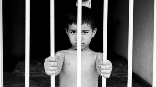 Free A poignant black and white portrait of a child holding bars, symbolizing isolation. Stock Photo