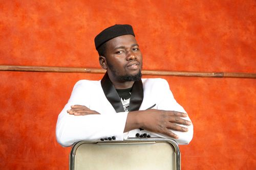 Free A confident man poses stylishly in a white suit with an orange background. Stock Photo
