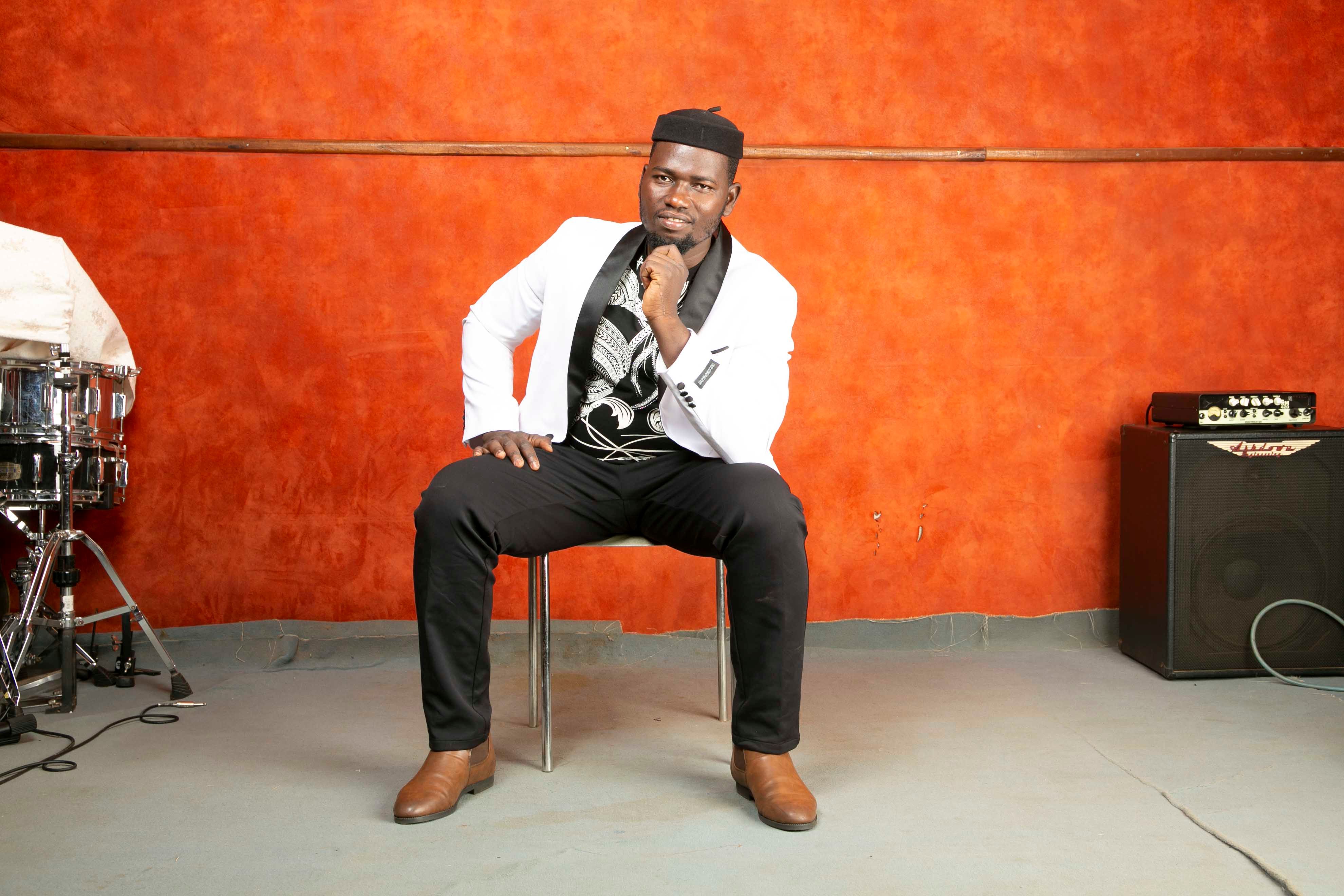Man in white jacket poses confidently in a vibrant music studio with instruments.