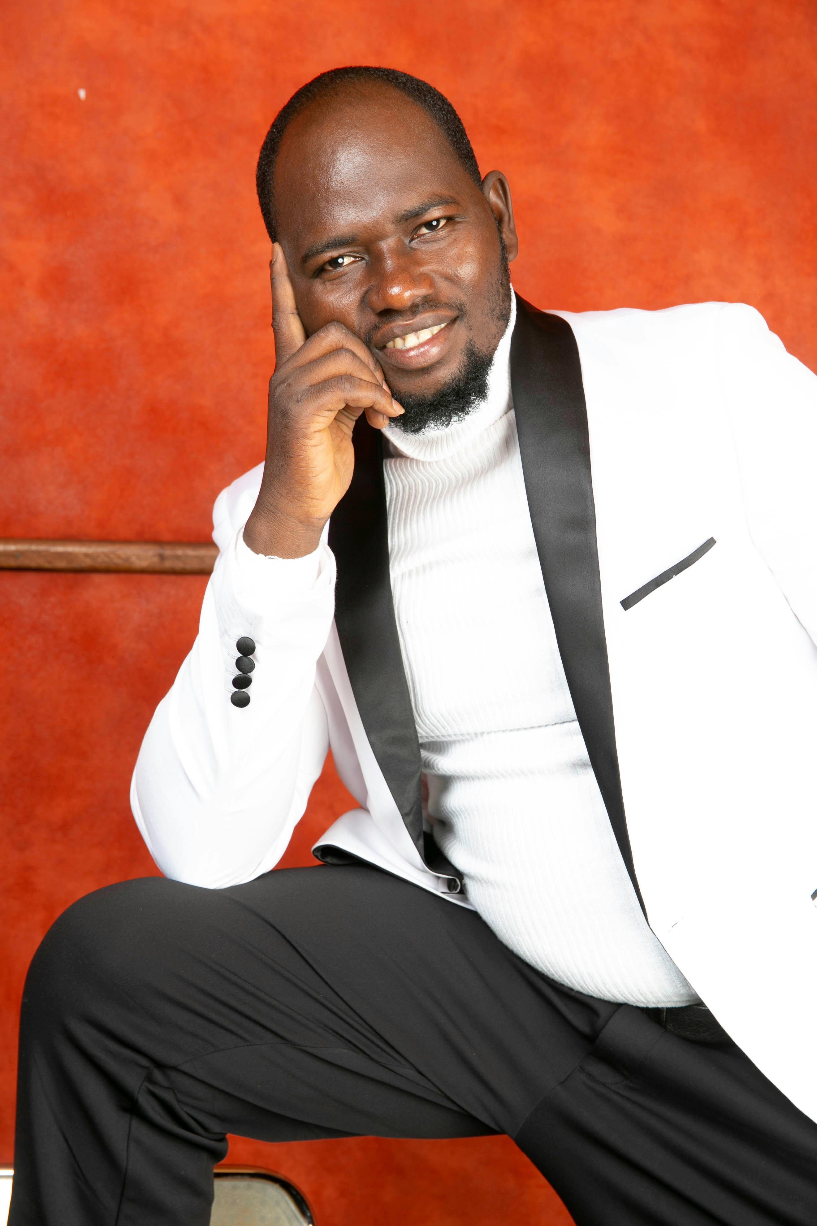Portrait of a confident man in a white suit posing against a bold orange background.