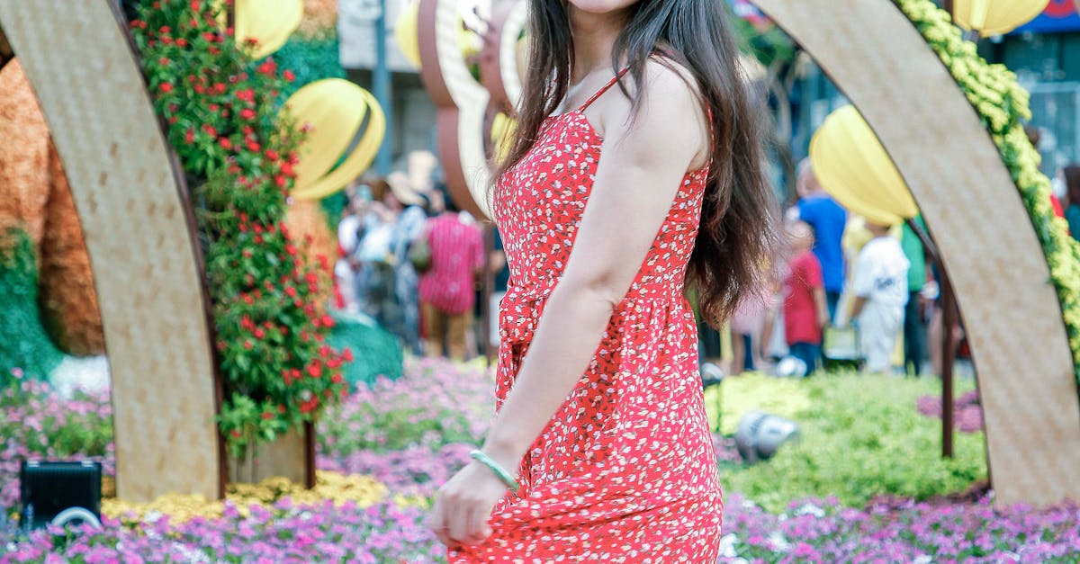 A joyful woman spins in a red dress surrounded by vibrant flowers outdoors.