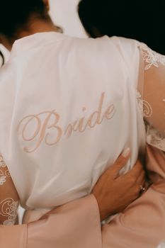 A bride wearing an embroidered white robe embraces a close friend before the wedding ceremony.
