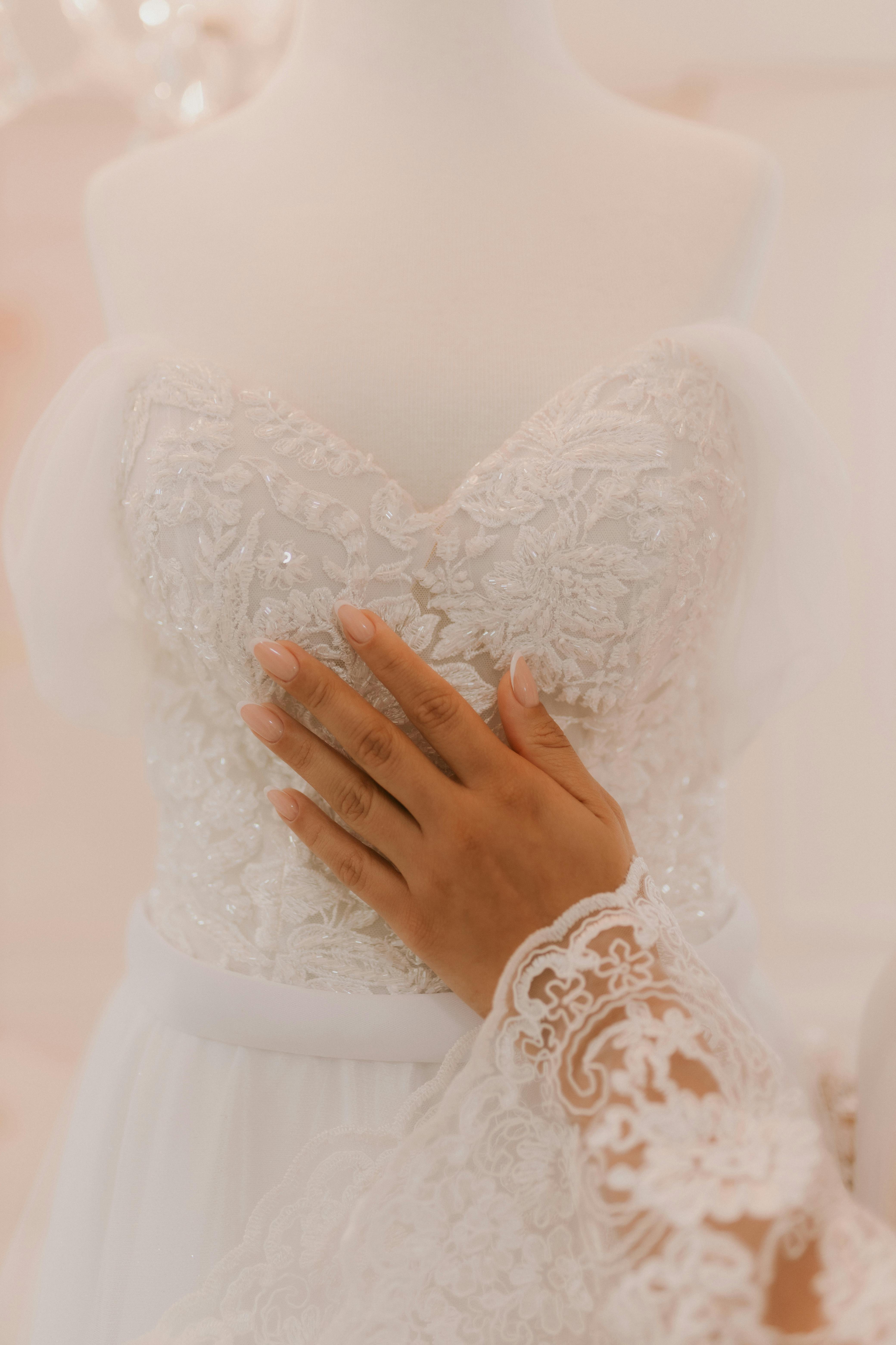 A hand touching a stunning lace wedding gown, showcasing intricate bridal fashion design.