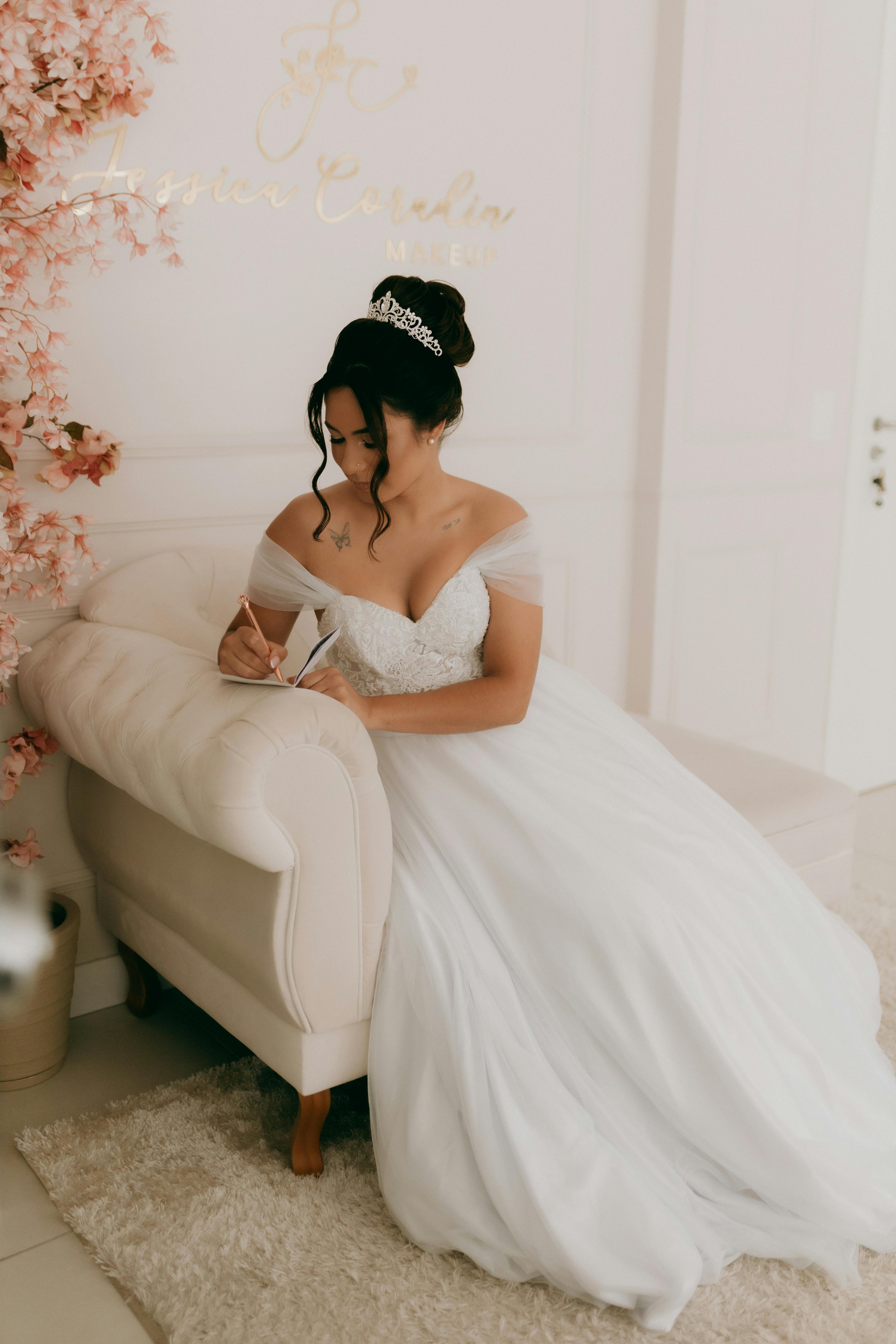 A beautiful bride in a white gown sits pensively in an elegant indoor setting.