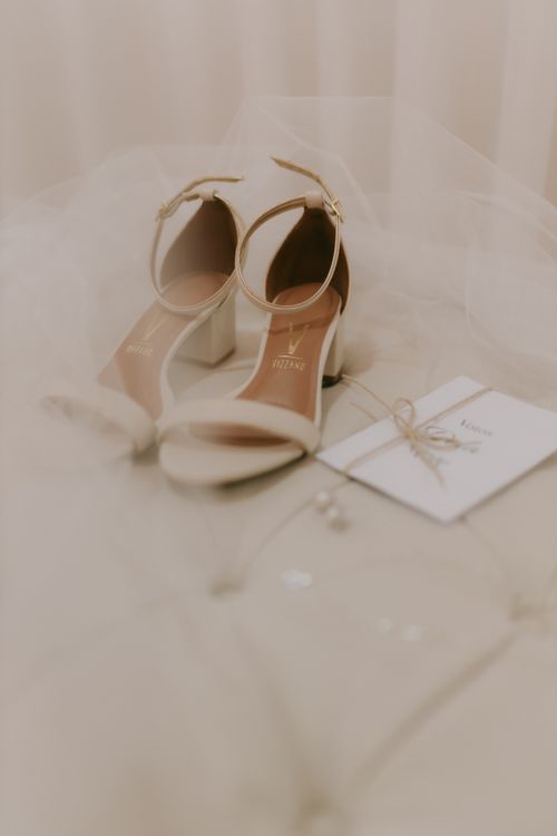Free Delicate white bridal shoes paired with a wedding invitation, set against a soft beige background. Stock Photo