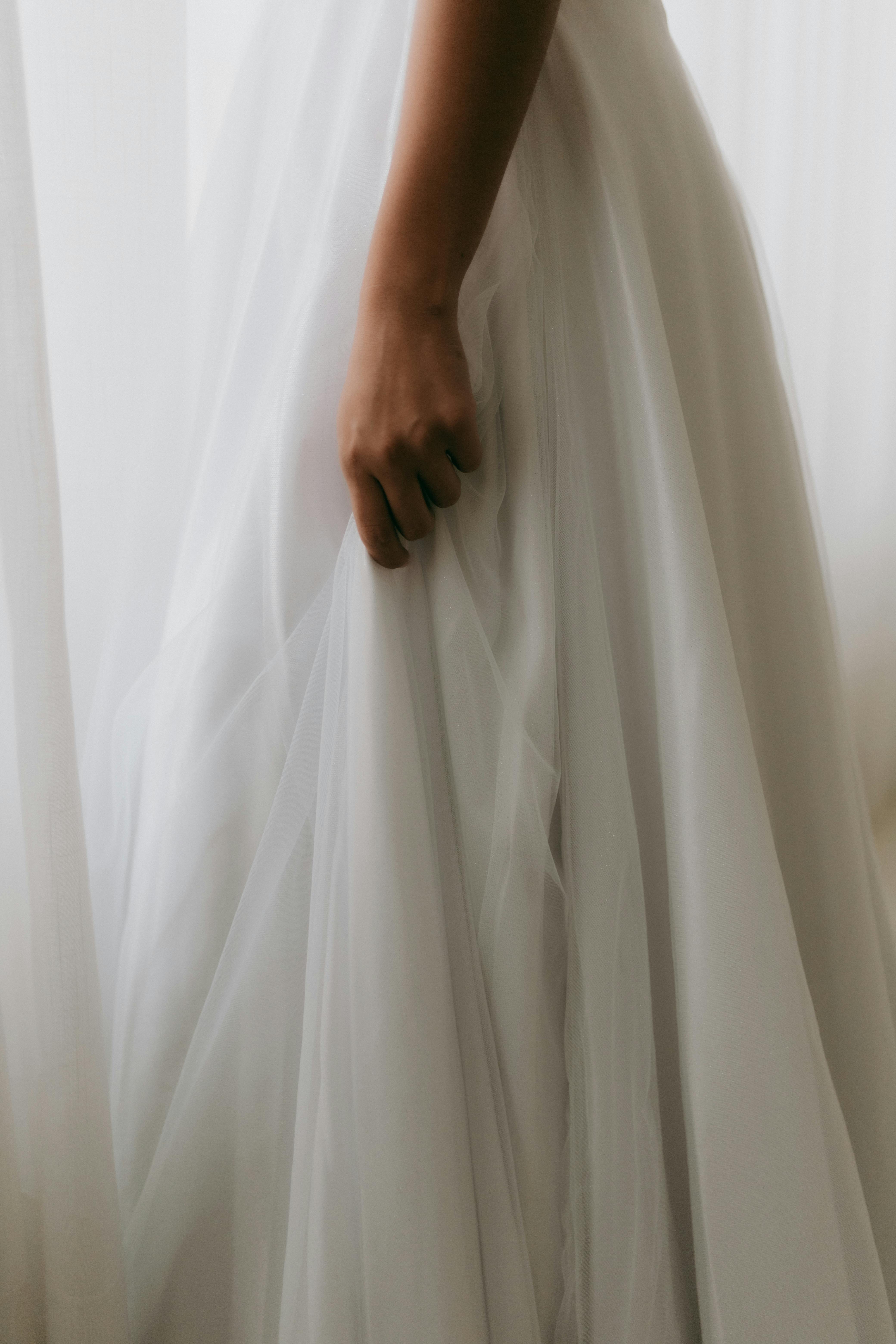 Graceful close-up of a bride holding her flowing white wedding dress with tulle.