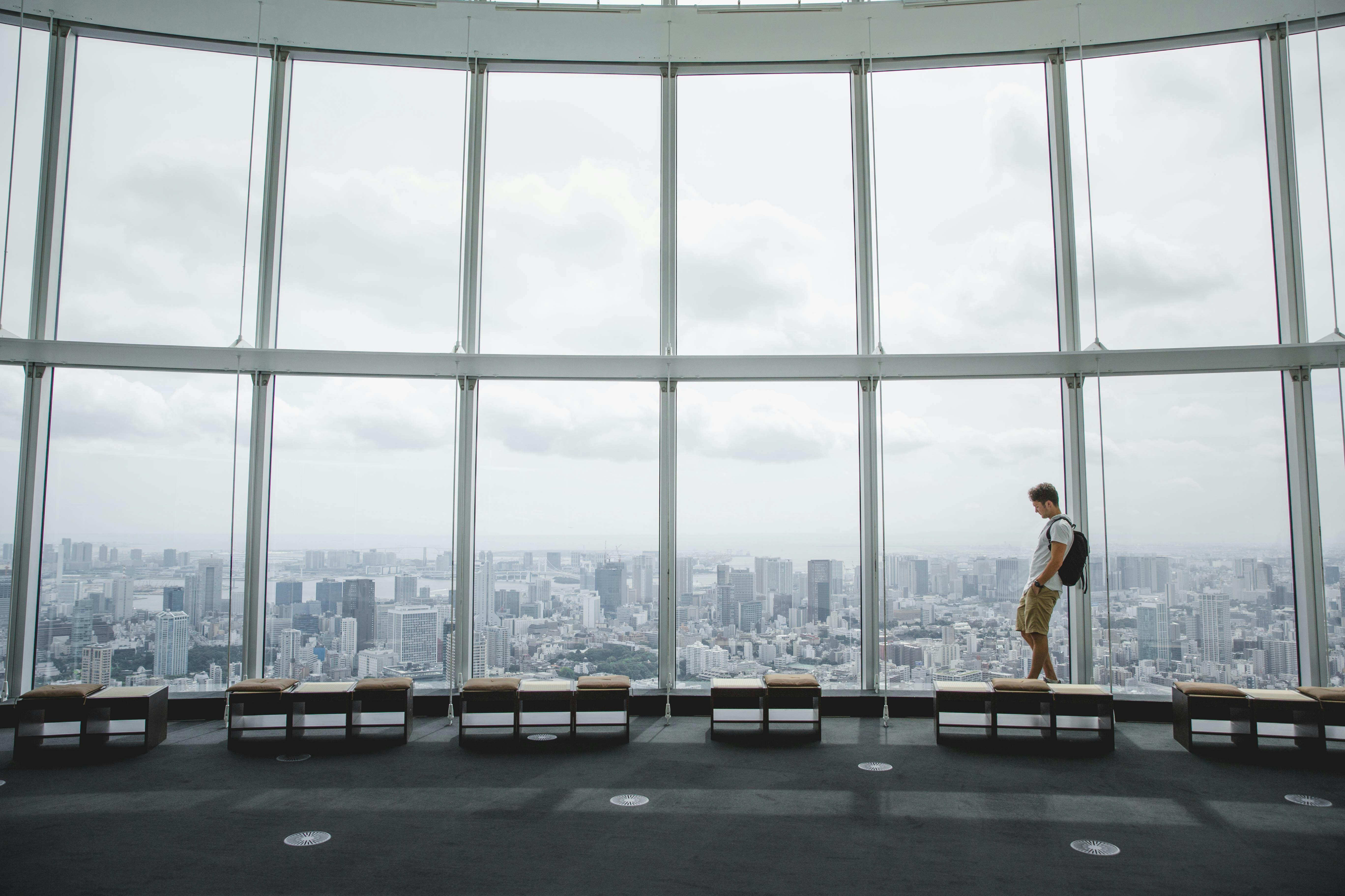 Man observing Tokyo skyline from a high-rise building with panoramic windows.
