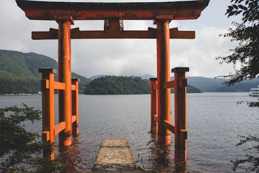 Iconic red torii gate at Lake Ashi in Hakone, Japan, surrounded by lush mountains and serene water.