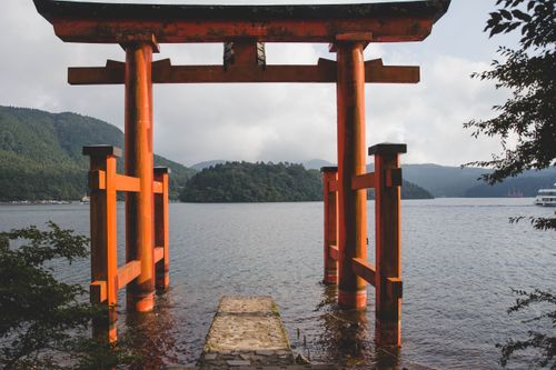 Free Iconic red torii gate at Lake Ashi in Hakone, Japan, surrounded by lush mountains and serene water. Stock Photo