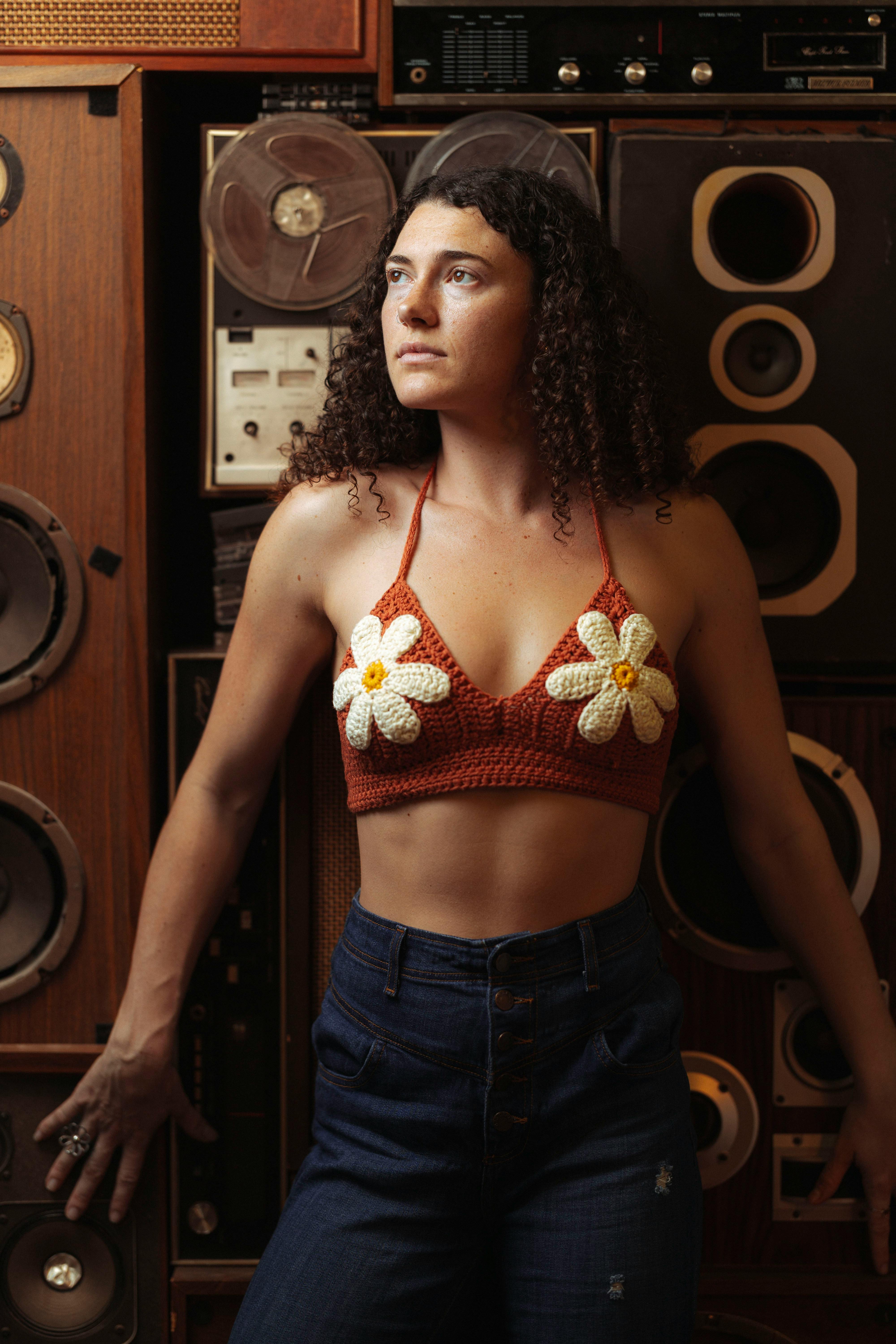 Stylish woman in crochet top poses confidently against a backdrop of vintage speakers.