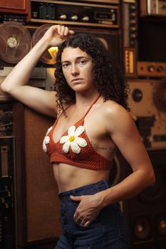 Woman in crochet top with flower design posing in front of vintage audio equipment.