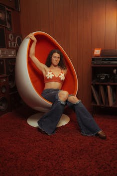 A woman in 70s-inspired attire sits in a vintage egg chair surrounded by retro decor.