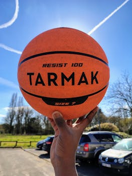 Orange basketball held outdoors with blue sky and contrails in the background.
