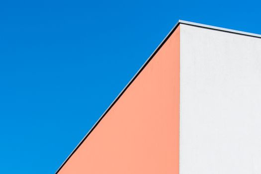 A minimalist view of a building's colorful corner against a clear blue sky.