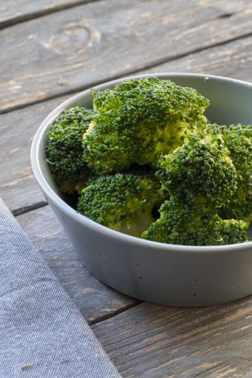 Free Fresh broccoli florets sit in a white bowl on a rustic wooden table surface, ready to enjoy. Stock Photo