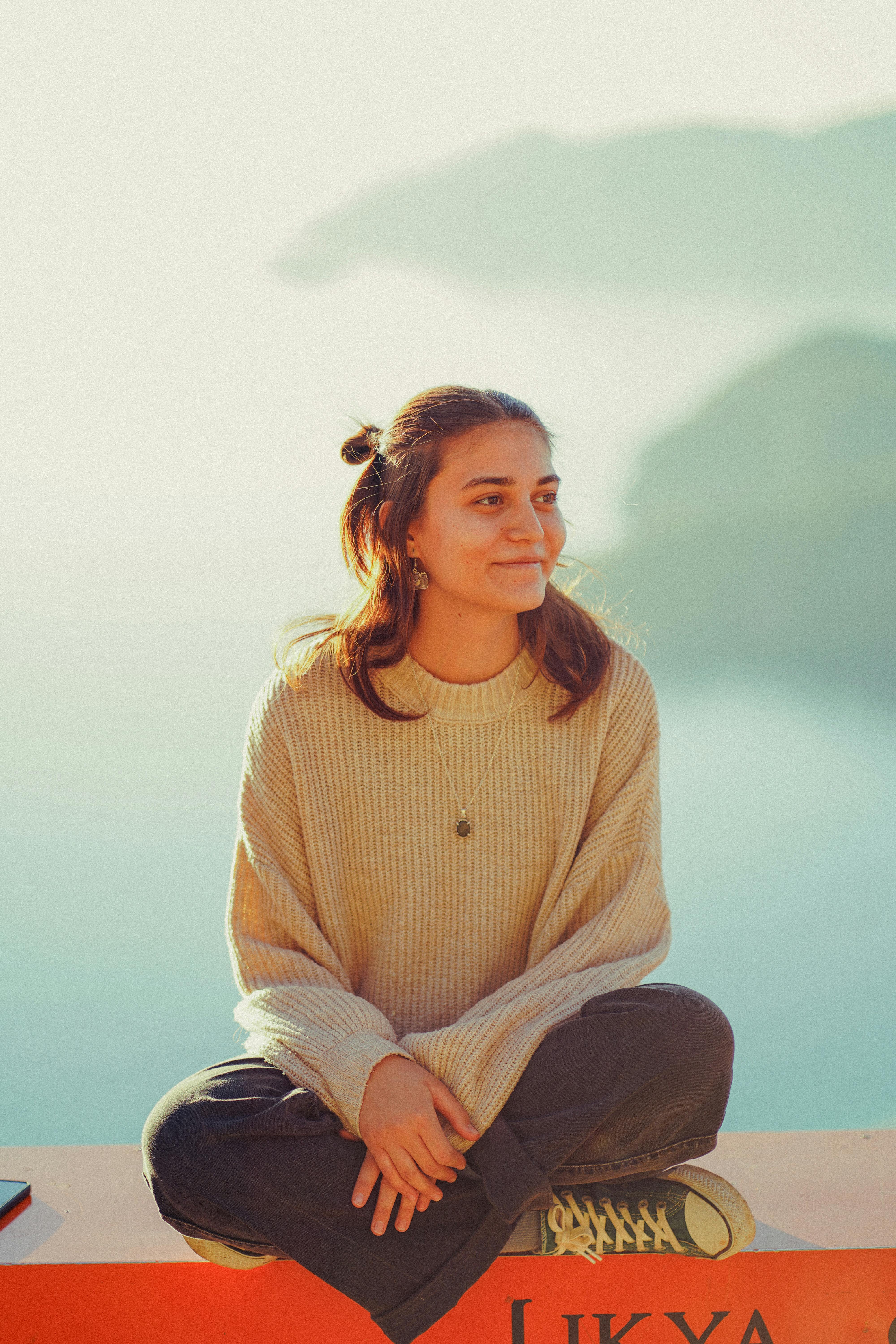 A young woman sitting cross-legged, enjoying a tranquil moment by the water's edge.