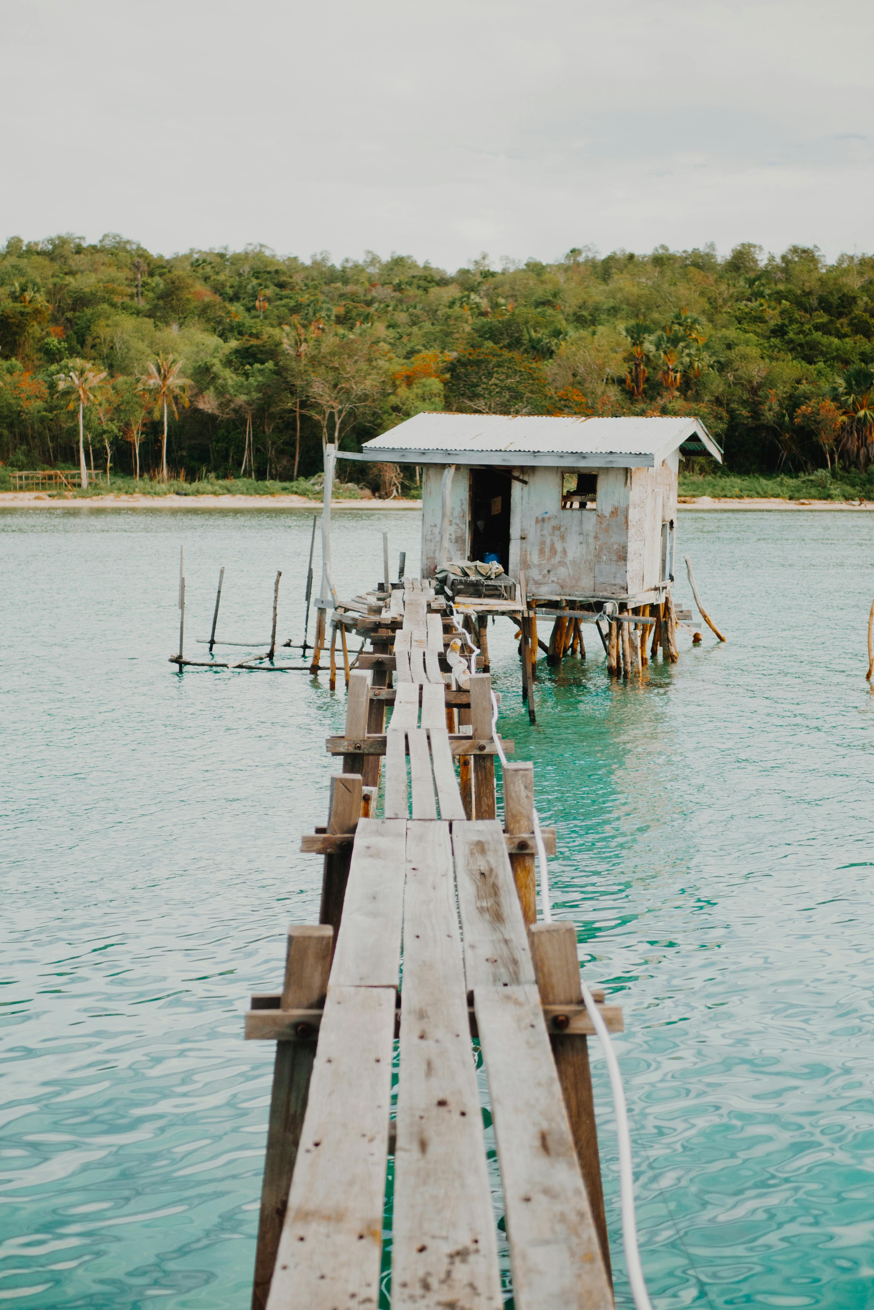 在马来西亚沙巴州，一座踩着高跷的乡村木屋旁，碧绿的水面上延伸着一条长长的木板路