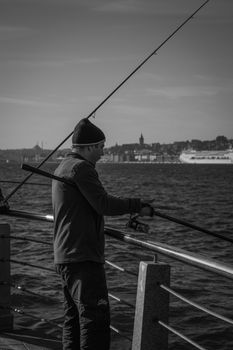 A fisherman casting a line in Istanbul, viewed from the waterfront with iconic cityscape behind.